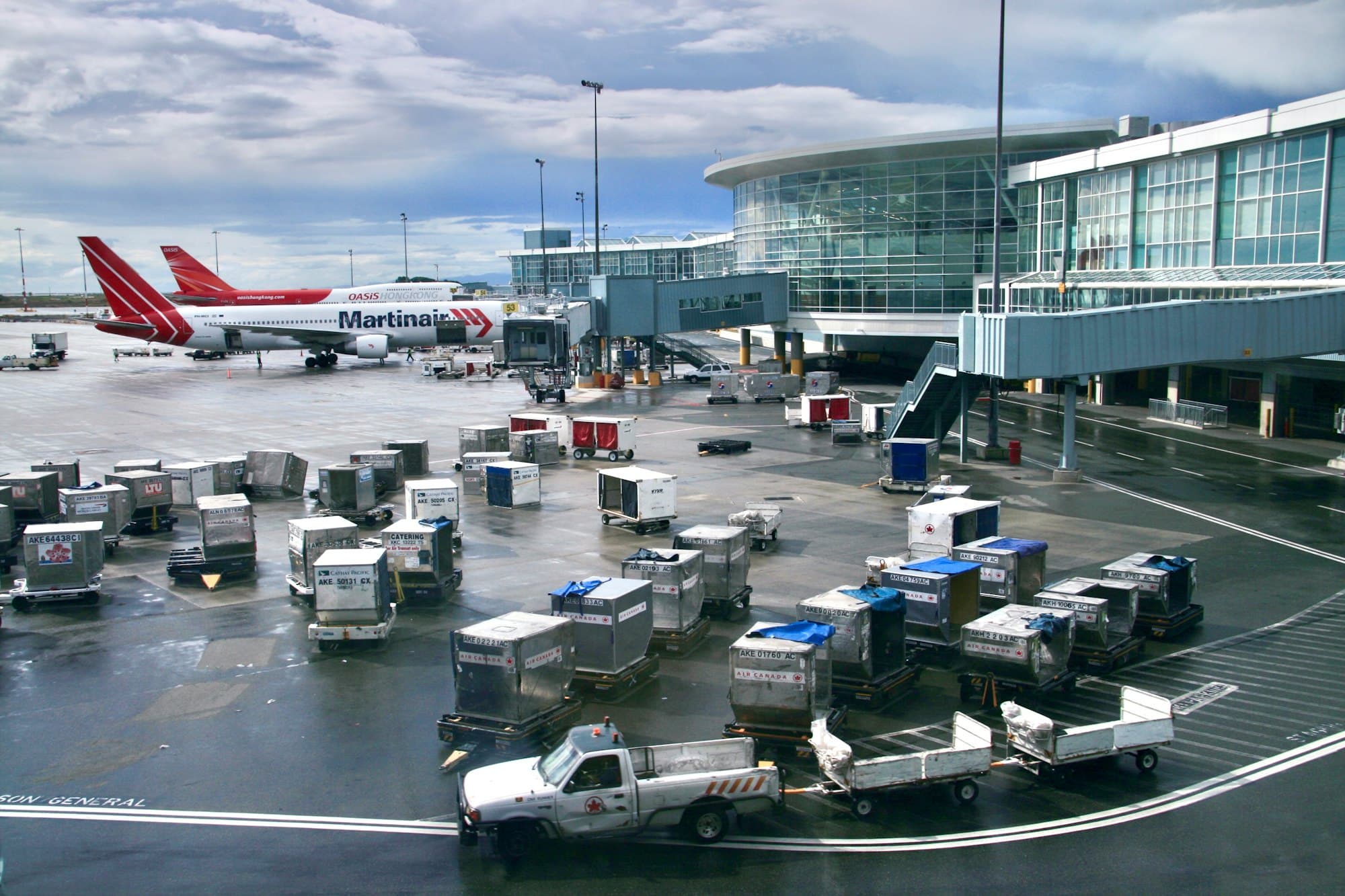 Baggage carts and a service truck on an airport apron, with aircraft and the terminal behind