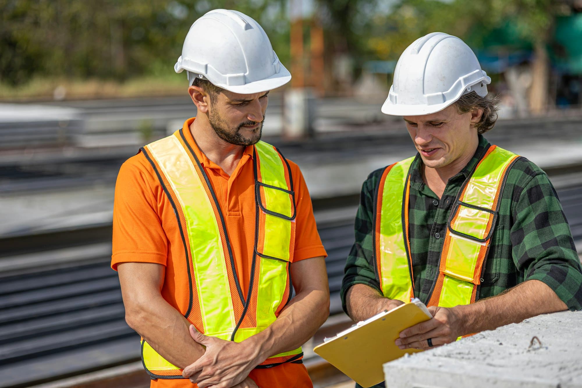 Two supervisors in hard hats and safety vests reviewing a clipboard on a job site