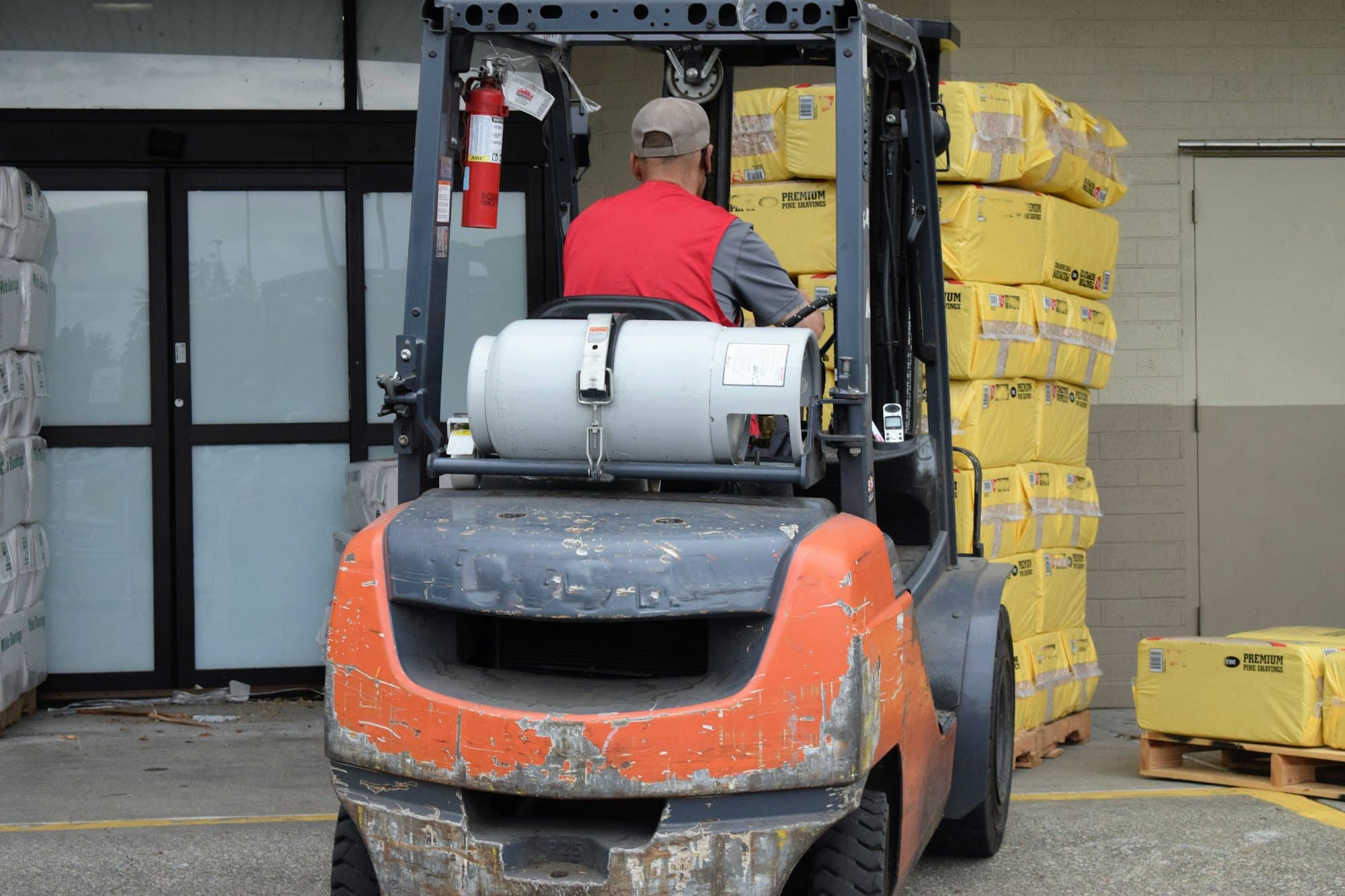 A forklift operator seen from behind, loaded with stacked pallets