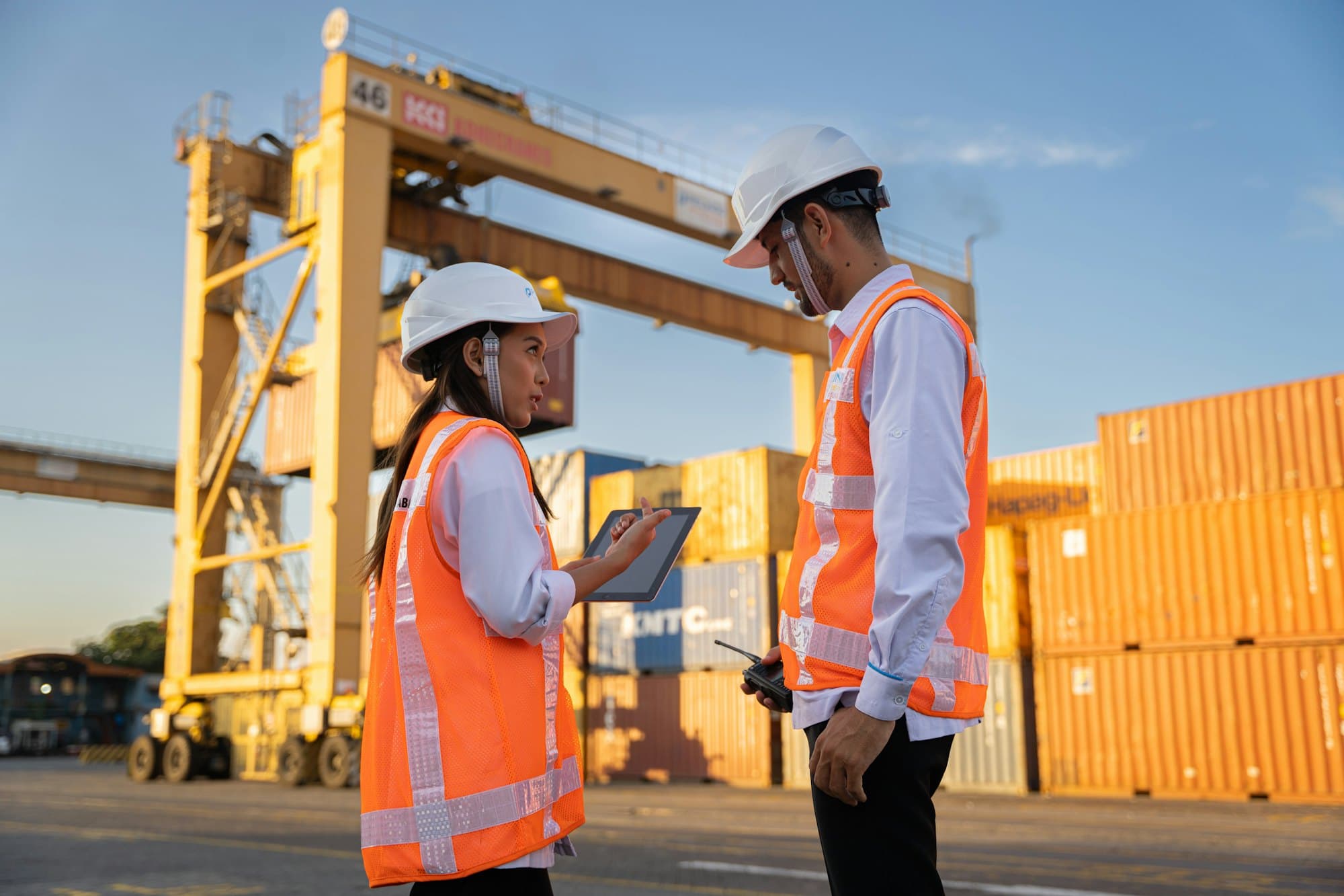 Two workers in high-visibility vests checking a tablet at a container port
