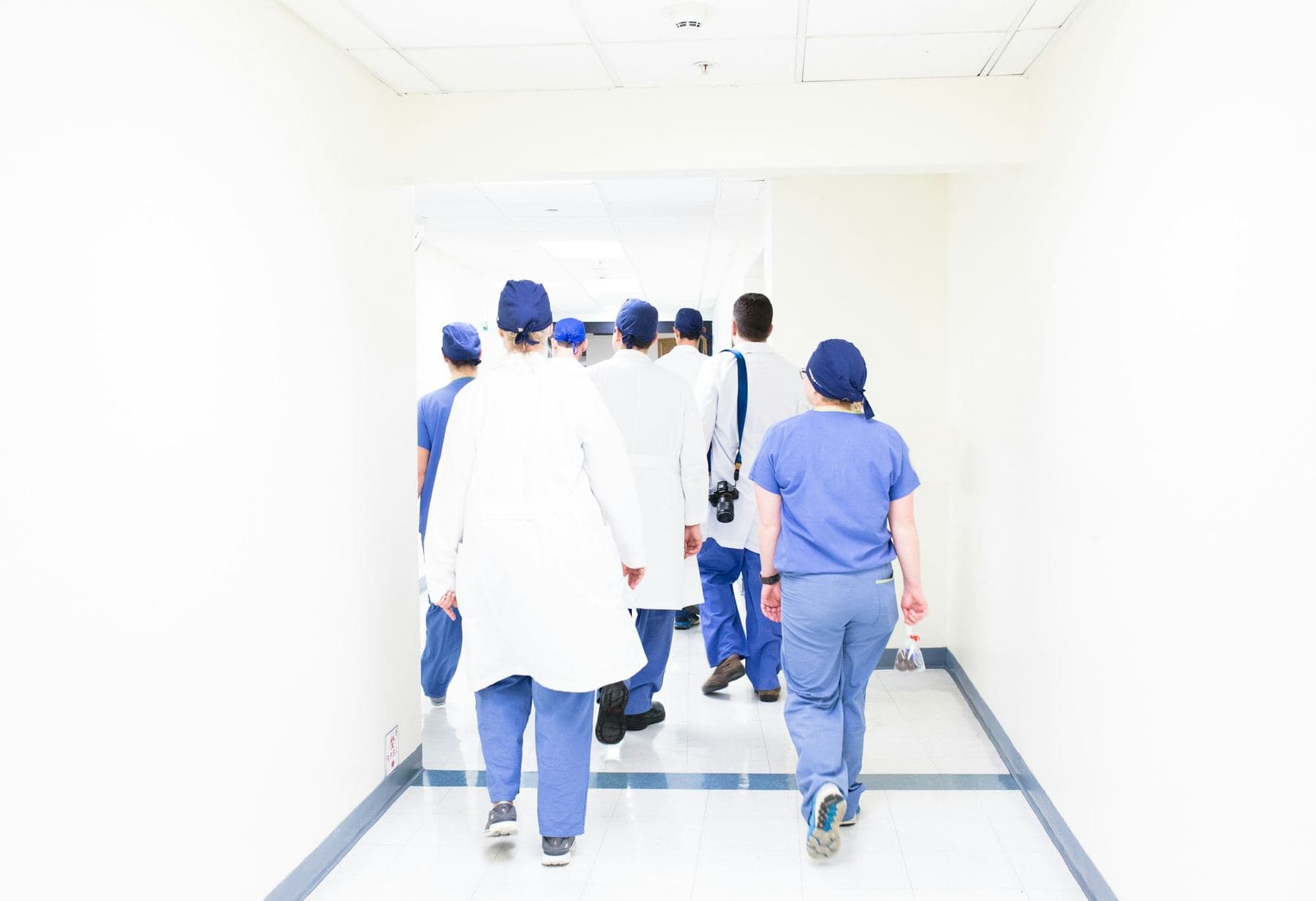 Hospital staff in scrubs and lab coats walking away down a bright hallway
