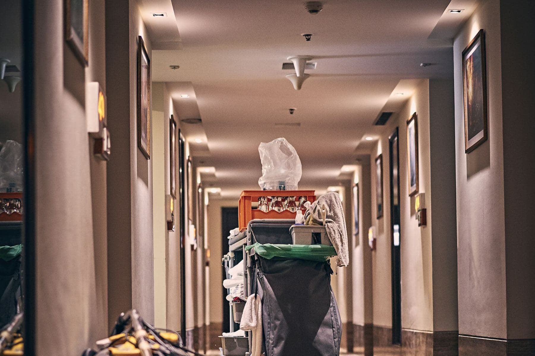 A housekeeping cart and vacuum in a long hotel corridor