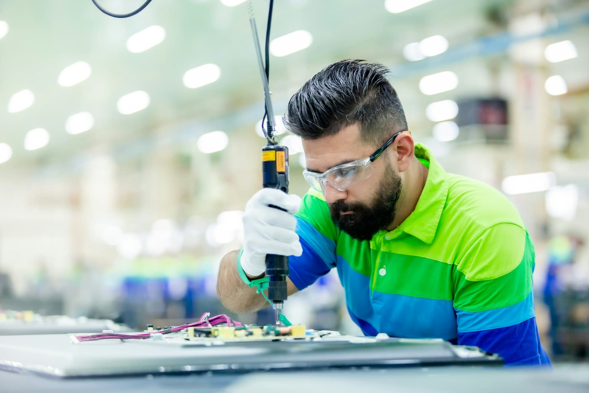 A technician in safety glasses and gloves assembling electronics on a factory floor