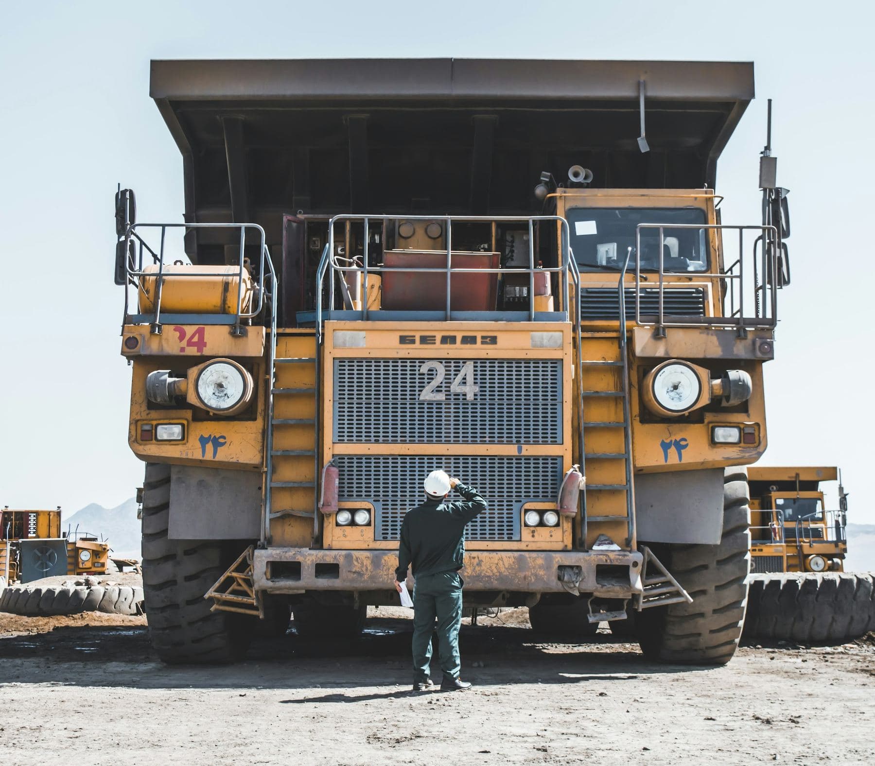A worker in a hard hat looking up at a large yellow haul truck in a quarry