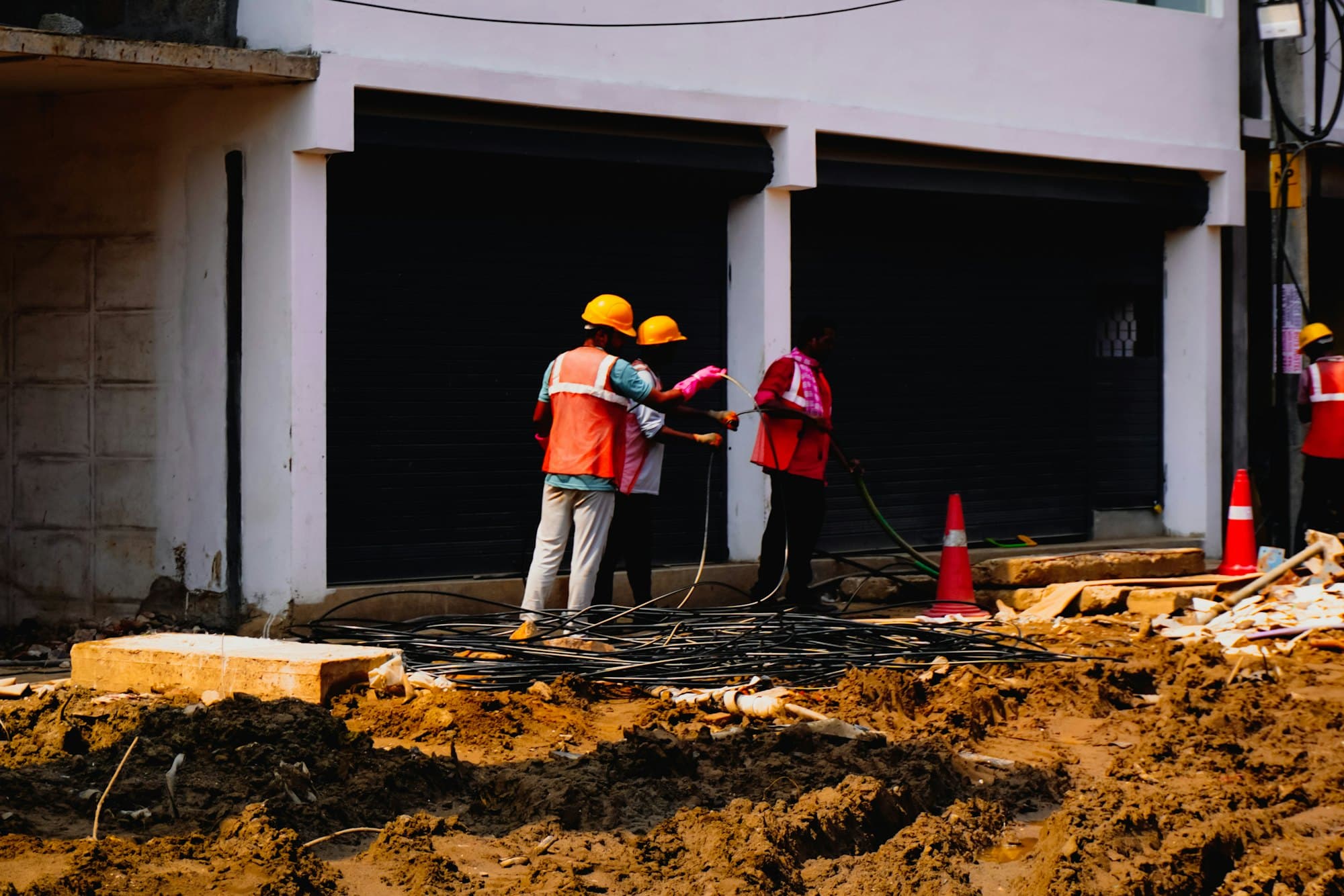 Workers in hard hats and vests near cones outside a building