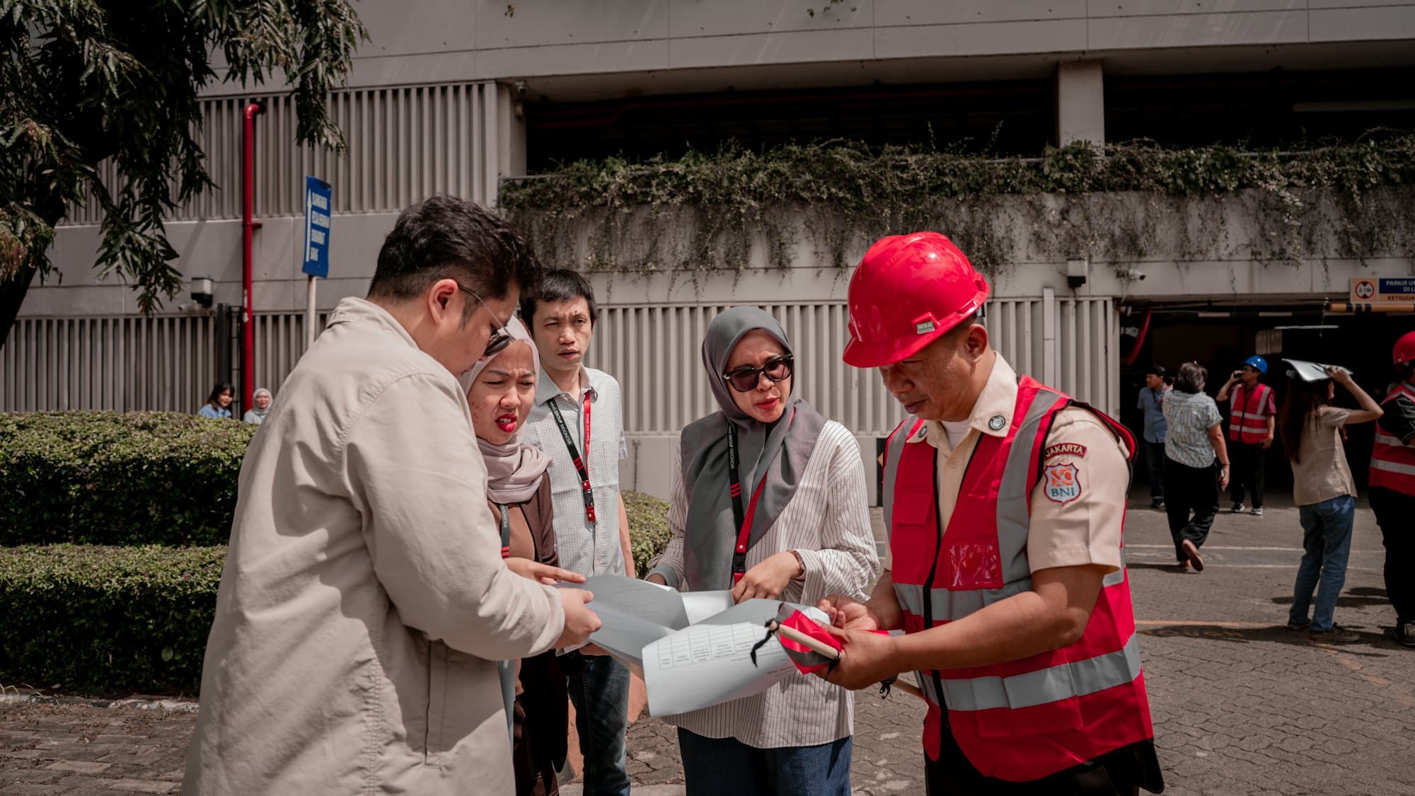 A supervisor in a red hard hat going over plans with colleagues outdoors