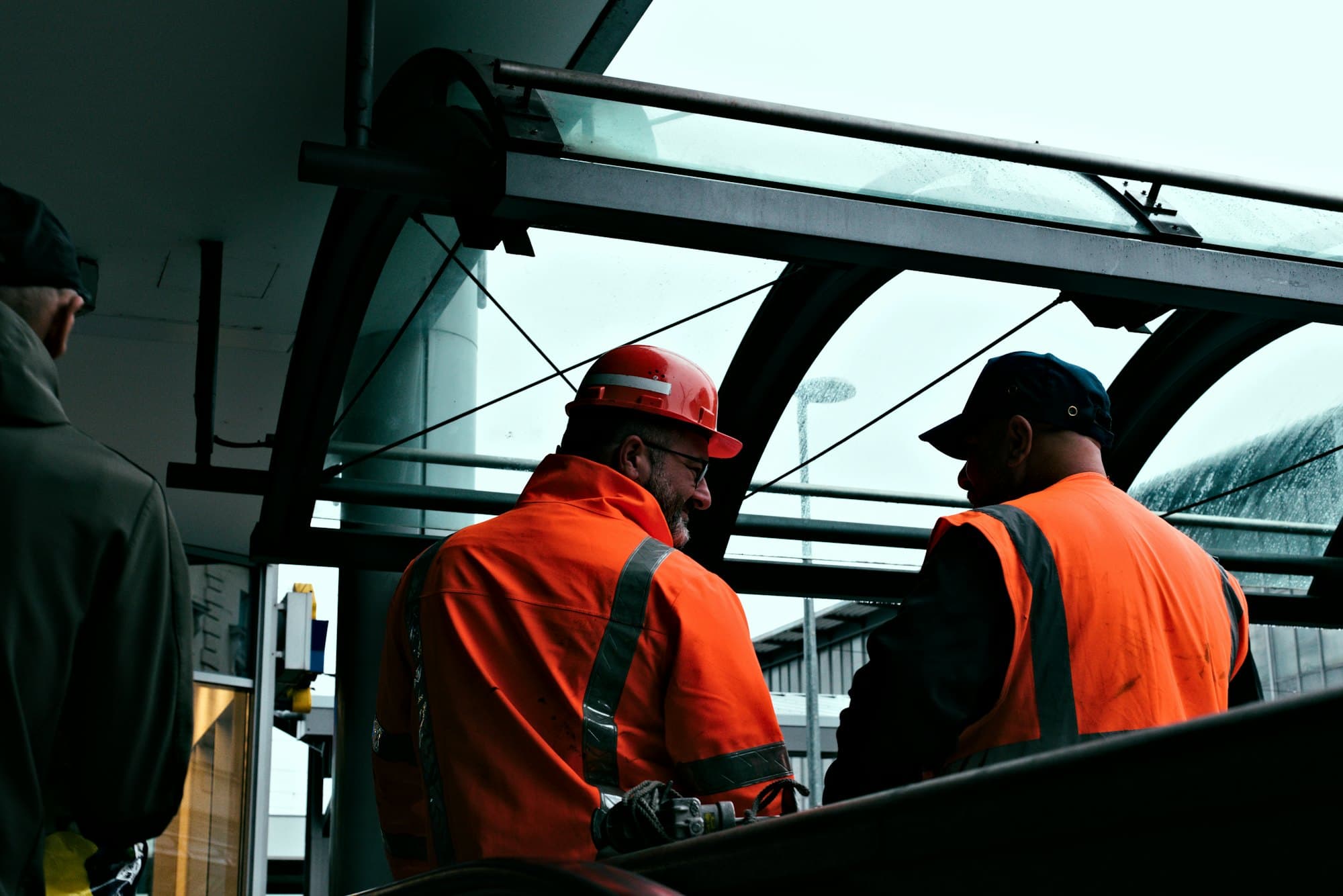 Two workers in orange high-visibility jackets talking, seen from behind